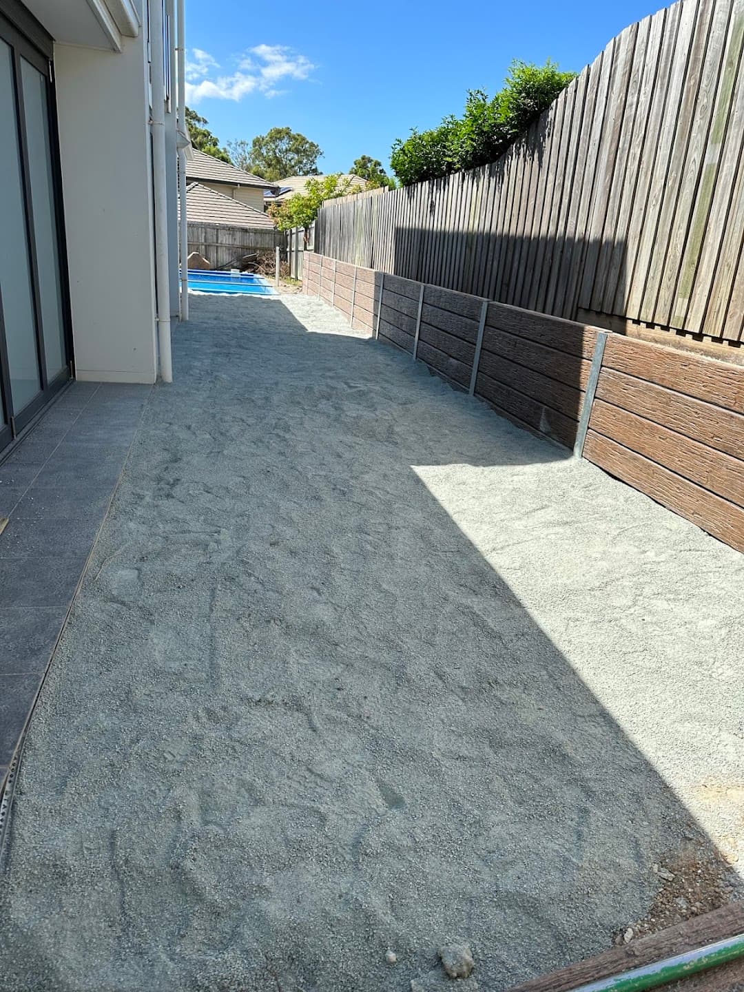 Compacted sand base along a sleeper wall ready for artificial turf