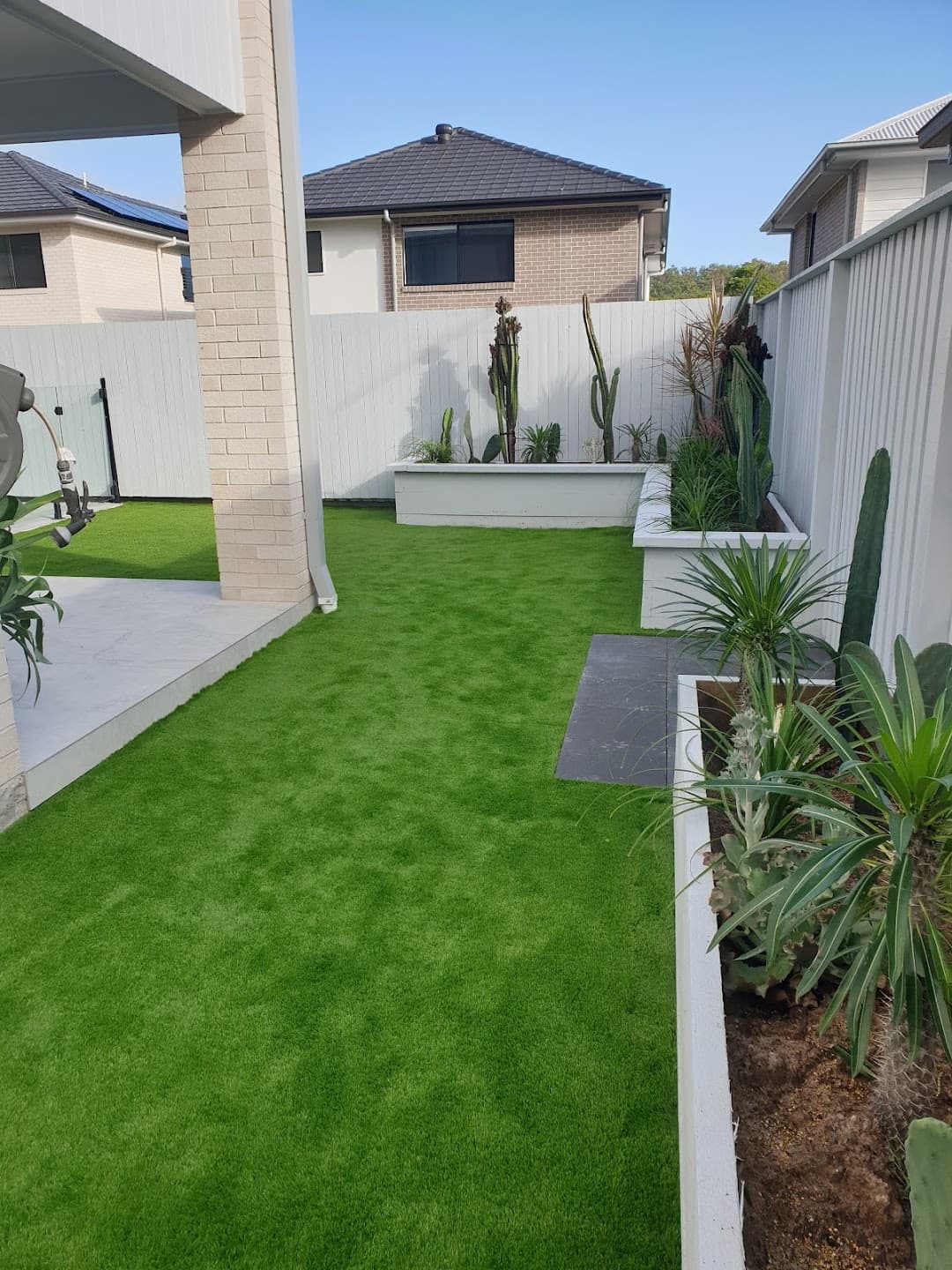 Narrow side yard with artificial turf and a raised rendered garden bed