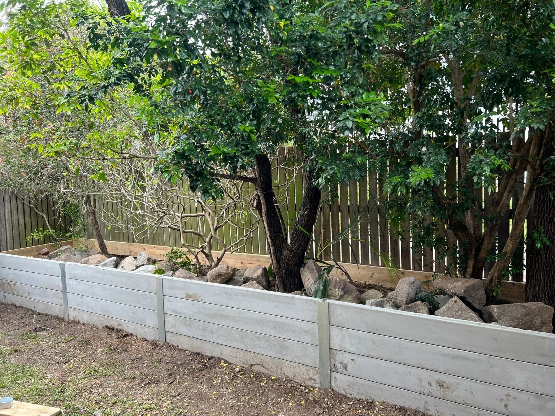 Grey concrete sleeper retaining wall holding a raised garden bed under a mature tree