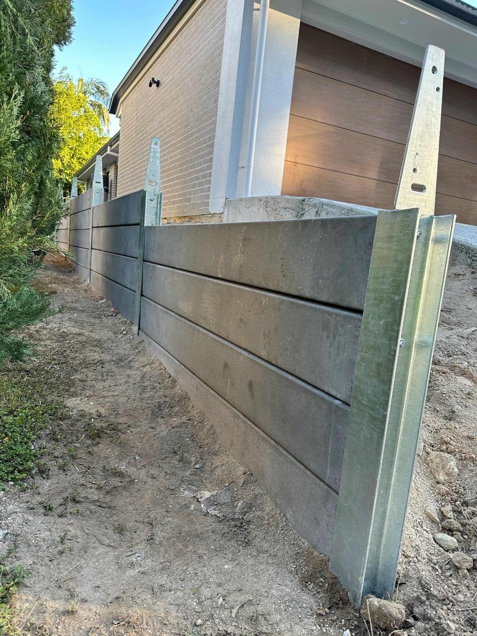 Concrete sleeper retaining wall with galvanised steel posts along a side boundary