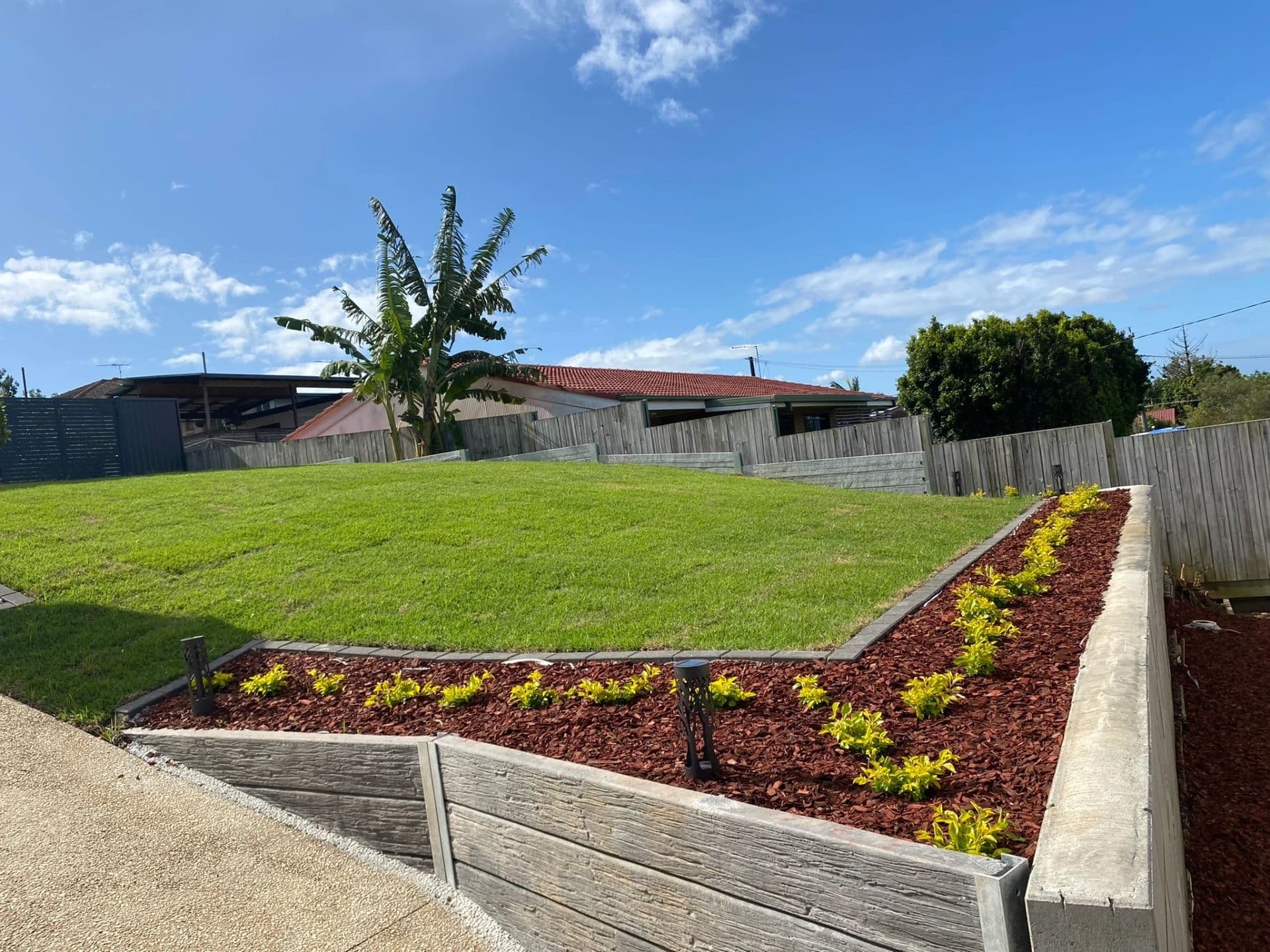 Tiered concrete sleeper retaining wall with mulched garden bed and turfed backyard